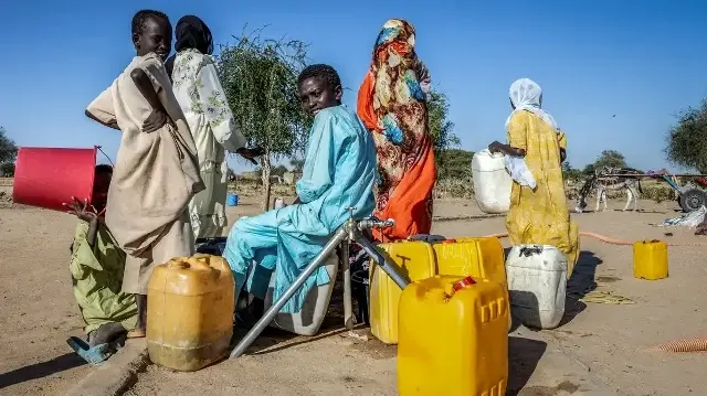 Des réfugiés soudanais remplissent des récipients d'eau à un point d'eau dans le camp de transit de Tine au Tchad, le 10 novembre 2025.
