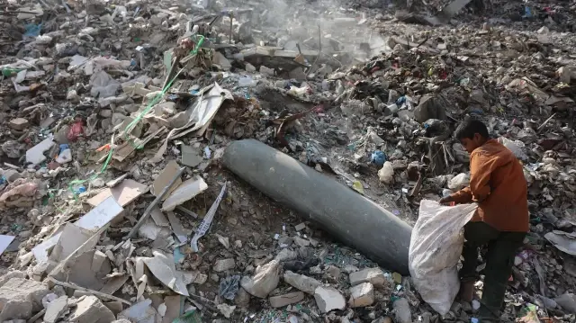Un garçon palestinien ramasse du plastique près d'un missile non explosé dans une décharge publique du quartier du marché Firas, à Gaza, le 12 novembre 2025.