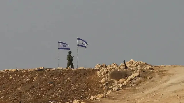 Un soldat israélien se tient à côté de drapeaux flottant au sommet d'une colline à Beit Ula, près d'Hébron, en Cisjordanie occupée, le 10 novembre 2025.