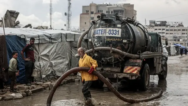 Un Palestinien nettoie l'eau stagnante sur la route près d'un camp de déplacés après les premières pluies hivernales à Gaza, le 14 novembre 2025.