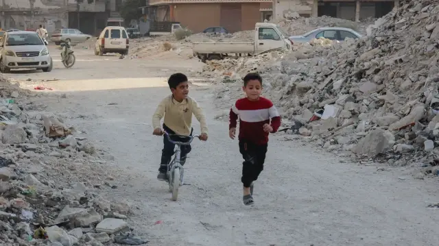 Des enfants jouent avec un vélo sur une route jonchée de débris dans le camp de Yarmouk, près de Damas, en Syrie, le 8 novembre 2025.