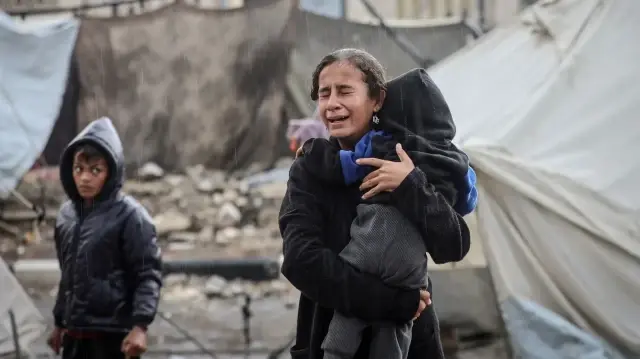 Une fillette palestinienne pleure, un bébé dans les bras, sous la pluie, alors que les Palestiniens, dont les maisons ont été détruites lors des deux années d'attaques israéliennes, connaissent des moments difficiles après que leurs tentes de fortune ont été inondées par les pluies torrentielles qui se sont abattues sur la ville de Gaza, le 14 novembre 2025. L'arrivée du froid et des précipitations a rendu les conditions de vie encore plus difficiles pour les habitants vivant dans des tentes de fortune.