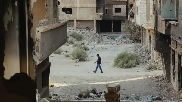 Un homme marche dans une rue endommagée, encadrée par les vestiges de bâtiments détruits dans le camp de Yarmouk, à Damas, en Syrie, le 8 novembre 2025.