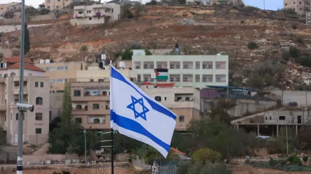 Un drapeau palestinien est visible sur un bâtiment situé en face d'un drapeau national israélien placé à l'entrée du village d'As-Sawiyah, au sud de Naplouse, en Cisjordanie occupée, le 16 novembre 2025.