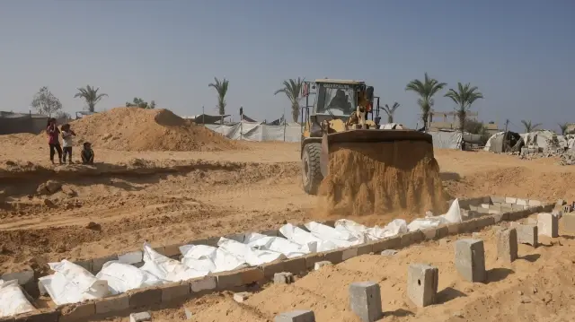 Des enfants regardent une pelleteuse recouvrir de sable les corps de Palestiniens lors d'un enterrement collectif dans un cimetière de Khan Yunis, dans le sud de la bande de Gaza, le 10 novembre 2025.