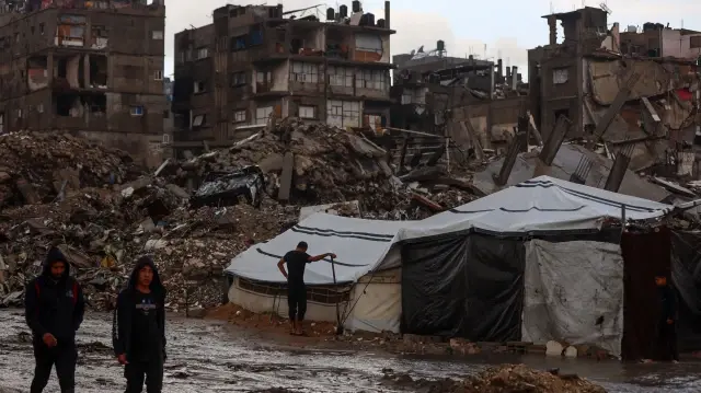 Des Palestiniens marchent sous la pluie dans un camp de fortune à Gaza, le 25 novembre 2025. 