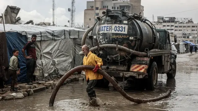 Un Palestinien nettoie l'eau stagnante sur la route près d'un camp de déplacés après les premières pluies hivernales à Gaza, le 14 novembre 2025.