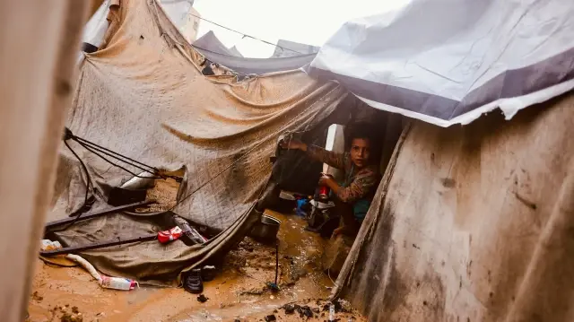 Un enfant palestinien assis dans une tente sous la pluie, dans un camp de fortune abritant des Palestiniens déplacés à Deir al-Balah, dans le centre de la bande de Gaza, le 25 novembre 2025.