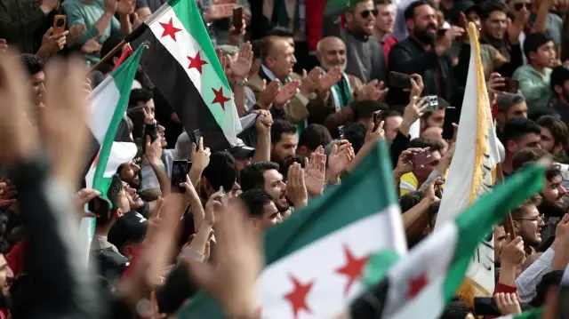 Des personnes brandissent des drapeaux alors qu'elles se rassemblent sur une place pour commémorer le 10e anniversaire de la prise d'Idlib par les forces d'opposition à l'armée de l'ancien président Bachar al-Assad en 2015, dans la ville d'Idlib, au nord de la Syrie, le 28 mars 2025. 