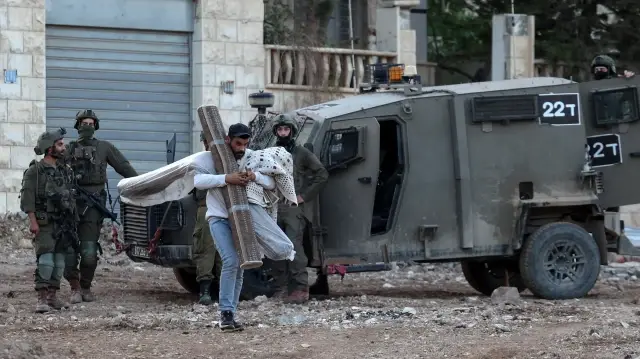 Un Palestinien transporte ses affaires alors qu'il évacue son domicile lors d'un raid de l'armée israélienne dans la banlieue du camp de réfugiés de Jénine, en Cisjordanie occupée, le 27 novembre 2025.