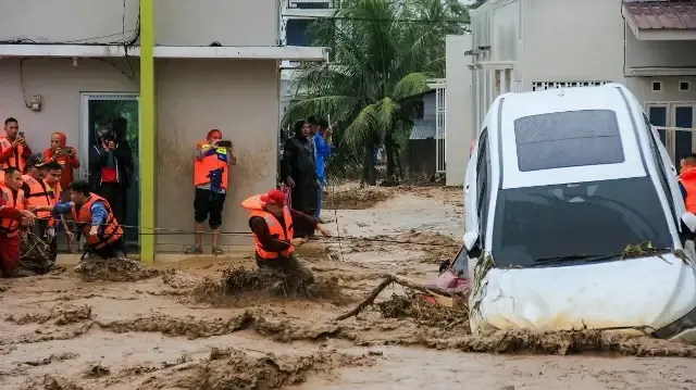 Des sauveteurs pataugent dans les eaux de crue en s'agrippant à une corde pour évacuer les habitants bloqués dans leurs maisons à Padang, dans la province de Sumatra occidental, le 27 novembre 2025.
