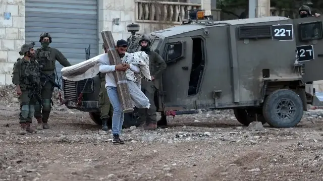 Un Palestinien transporte ses affaires alors qu'il évacue son domicile lors d'un raid de l'armée israélienne dans la banlieue du camp de réfugiés de Jénine, en Palestine occupée, le 27 novembre 2025.