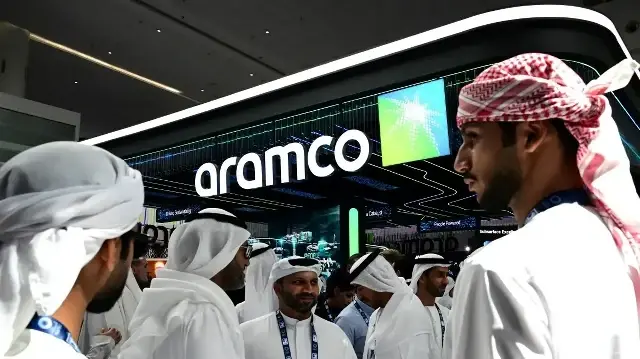 Des invités se tiennent devant le stand de l'ARAMCO (officiellement la Saudi Arabian Oil Company) lors du Salon international du pétrole et de la conférence d'Abu Dhabi (ADIPEC) à Abu Dhabi, le 3 novembre 2025.
