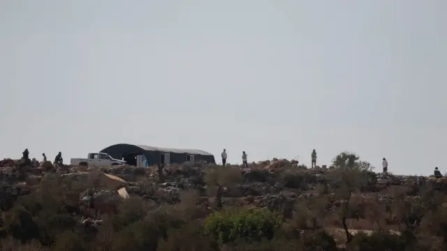 Des colons israéliens se tiennent au sommet d'une colline et observent des agriculteurs et des bénévoles palestiniens récolter des olives près du village de Baita, au sud de Naplouse, en Cisjordanie occupée, le 1er novembre 2025.