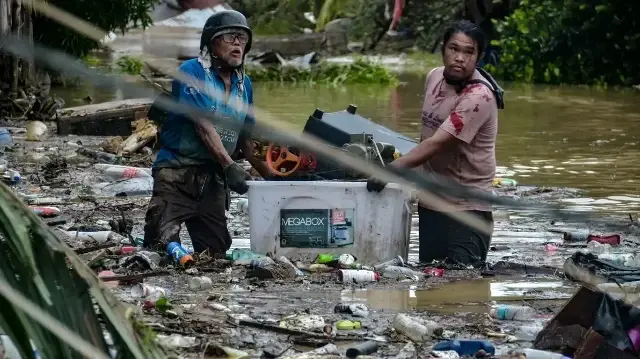 Des habitants transportant leurs effets personnels pataugent dans une rue inondée alors qu'ils évacuent leurs maisons submergées dans la ville de Liloan, province de Cebu, le 4 novembre 2025, après le passage du typhon Kalmaegi pendant la nuit.