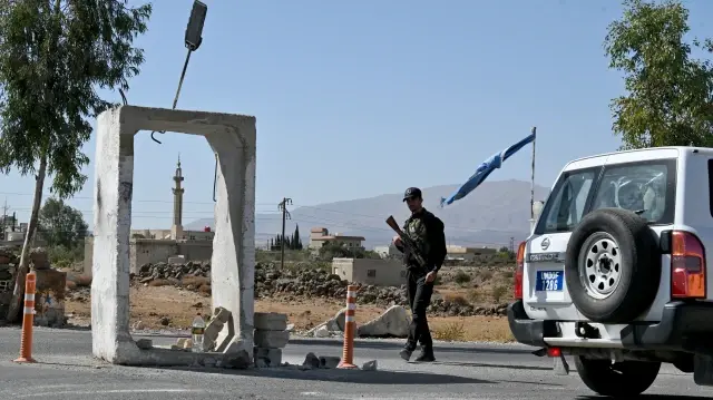 Un véhicule de la Force des Nations Unies chargée d'observer le dénouement du conflit (FNUOD) passe devant un membre des forces de sécurité syriennes qui monte la garde devant une ancienne base militaire près de la ville de Quneitra, dans le sud de la Syrie, à la lisière du plateau du Golan annexé par Israël, le 21 septembre 2025.