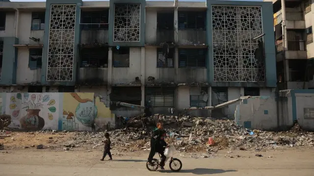 Un garçon fait du vélo avec un autre près d'un camp pour Palestiniens déplacés dans une école transformée en refuge dans le quartier d'Al-Rimal à Gaza, le 5 novembre 2025.