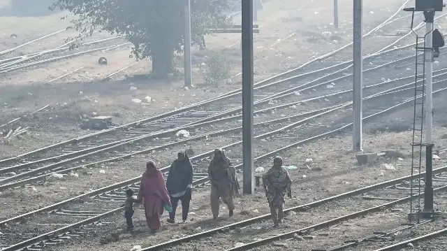 Des femmes accompagnées d'un enfant marchent le long d'une voie ferrée jonchée de détritus, dans un épais brouillard de pollution, à Lahore, le 1er décembre 2025.