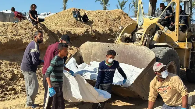 Des ouvriers déchargent les corps des victimes palestiniennes, enveloppés dans des linceuls blancs, de la benne d'une chargeuse et les déposent dans une fosse commune à Deir el-Balah, dans la bande de Gaza, le 1er décembre 2025.