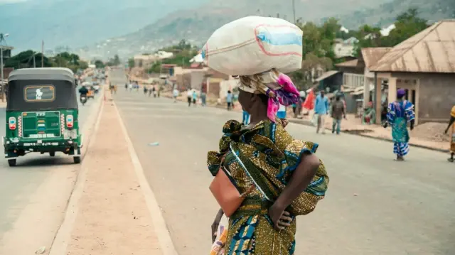 Une femme transporte un sac de farine sur la tête en traversant une route à Uvira, le 9 décembre 2025. Le Burundi a fermé sa frontière merdredi avec la République démocratique du Congo (RDC), où le groupe M23, soutenu par l’armée rwandaise, poursuit sa progression rapide vers Uvira.