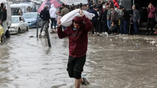 Un homme porte un sac tout en marchant dans les eaux de crue dans un campement de fortune abritant des Palestiniens déplacés à la suite de fortes pluies à Gaza, le 25 novembre 2025.