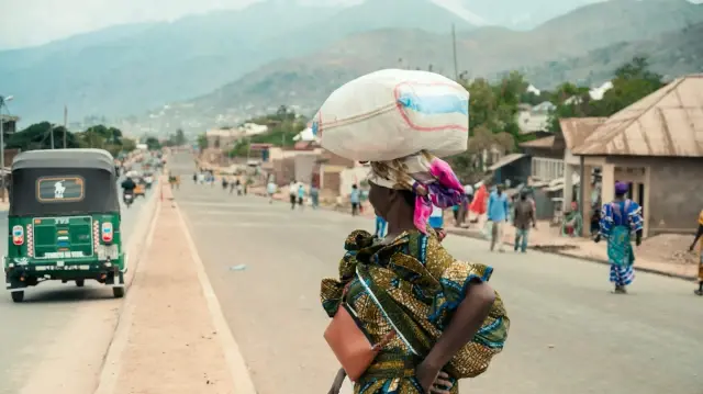 Une femme porte un sac de farine sur la tête alors qu'elle traverse une route à Uvira, le 9 décembre 2025. Des combats intenses ont lieu mardi dans l'est de la République démocratique du Congo (RDC), où le groupe M23, soutenu par l'armée rwandaise, poursuit son avancée rapide vers Uvira, une ville congolaise stratégique située près de la frontière avec le Burundi voisin et désormais menacée. 
