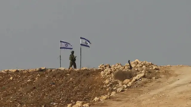Un soldat israélien se tient à côté de drapeaux flottant au sommet d'une colline à Beit Ula, près d'Hébron, en Cisjordanie occupée, le 10 novembre 2025.
