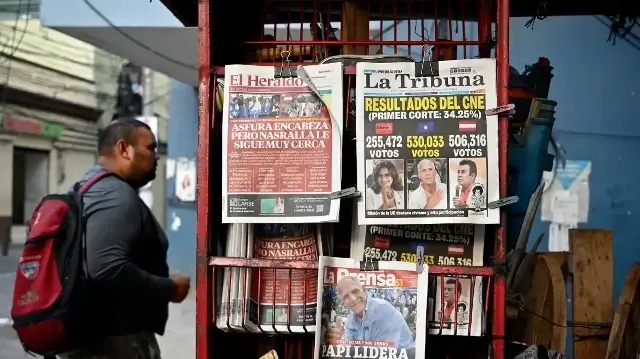 Un homme passe devant un kiosque affichant les premières pages des journaux à Tegucigalpa, le 1er décembre 2025, au lendemain des élections nationales. Le candidat Nasry Asfura, soutenu par le président américain Donald Trump, et son rival Salvador Nasralla, également issu de la droite, sont au coude à coude dans la course à la victoire aux élections présidentielles du Honduras lundi.