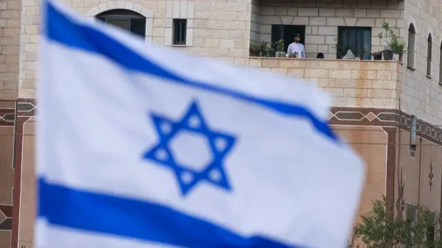 Un drapeau palestinien est visible sur un bâtiment situé en face d'un drapeau national israélien placé à l'entrée du village d'As-Sawiyah, au sud de Naplouse, en Cisjordanie occupée, le 16 novembre 2025.