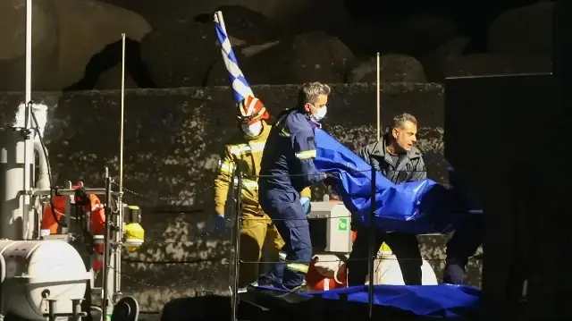 Des pompiers et des membres des garde-côtes helléniques transportent des sacs contenant des corps depuis un navire des garde-côtes après le naufrage d'un bateau de migrants au large du port d'Ierapetra, sur l'île de Crète, le 6 décembre 2025.