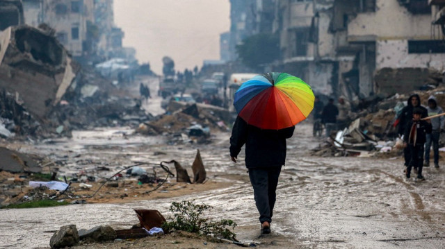 Un palestinien marche avec un parapluie aux couleurs de l'arc-en-ciel dans une rue boueuse, au milieu des décombres de bâtiments détruits et lourdement endommagés par les frappes israéliennes, dans le nord de la ville de Gaza, le 10 février 2025.