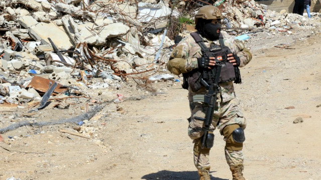 Un soldat libanais monte la garde devant un tas de décombres alors que des personnes inspectent leurs maisons détruites dans le village d'Adaisseh, dans le sud du Liban, le 18 février 2025, suite au retrait des troupes israéliennes de la zone frontalière.