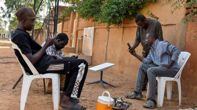 De jeunes Nigériens boivent du thé à côté d'une antenne satellite Starlink dans une rue de Niamey, le 22 janvier 2025. 