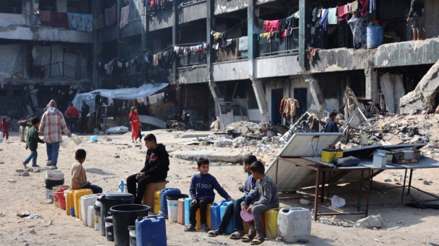 Des enfants palestiniens s'assoient et attendent à côté de bidons d'eau dans une école transformée en abri à Jabalia, dans le nord de la bande de Gaza, le 4 février 2025.