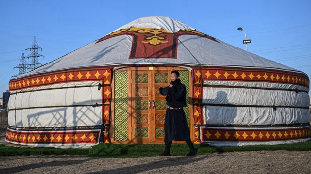 Un homme en costume traditionnel mongol se tient devant une yourte lors du "Mongols Nomadic Winter Festival" au parc national d'Oulan-Bator, la capitale de la Mongolie, le 20 février 2025.