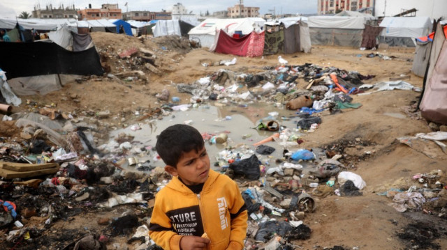 Un garçon palestinien se tient près de déchets et d'eau stagnante dans un camp pour personnes déplacées à Nuseirat, dans le centre de la bande de Gaza, le 23 février 2025.