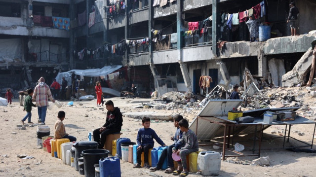 Des enfants palestiniens s'assoient et attendent à côté de bidons d'eau dans une école transformée en abri à Jabalia, dans le nord de la bande de Gaza, le 4 février 2025.