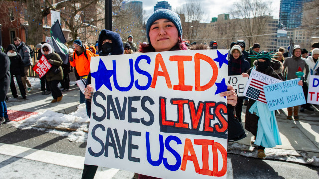 Une femme tient une pancarte soutenant l'USAID alors que des manifestants se rassemblent contre le président américain Donald Trump et ses politiques lors d'une manifestation près du Massachusetts Statehouse lors du Presidents' Day, le 17 février 2025, à Boston, Massachusetts.