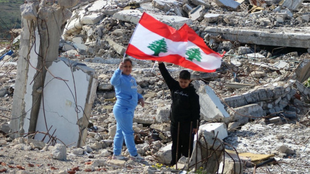 Des enfants libanais brandissent leur drapeau national en marchant sur les décombres d'un bâtiment détruit, dans le village de Marwahin, dans le sud du pays, près de la clôture frontalière avec Israël, le 28 janvier 2025.
