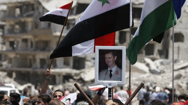 Un civil brandit un portrait du président syrien lors d'une cérémonie de levée du drapeau à l'entrée de Hajar al-Aswad, dans la banlieue sud de la capitale Damas, le 24 mai 2018.