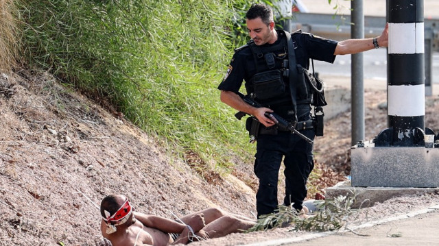 Un membre des forces de sécurité israéliennes se tient à côté d'un prisonnier palestinien aux yeux bandés à la frontière avec Gaza, près de la ville d'Ashkelon, dans le sud d'Israël, le 8 octobre 2023.