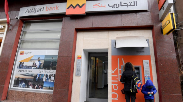 Un enfant se tient à côté d'une femme qui retire de l'argent à un distributeur automatique le 7 mars 2025 à Tunis. 