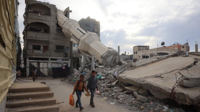 Des enfants palestiniens transportent de la nourriture devant des bâtiments détruits dans le camp de réfugiés de Nuseirat, dans le centre de la bande de Gaza, le 3 mars 2025, pendant le mois de jeûne musulman du Ramadan.
