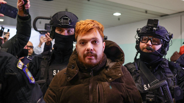 Le trafiquant de drogue français Mohamed Amra est escorté par des policiers à l'aéroport international Henri Coanda d'Otopeni, près de Bucarest, en Roumanie, le 25 février 2025, où il a été placé dans un avion en vue de son extradition vers la France.