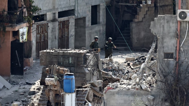 Des soldats israéliens regardent une pelleteuse militaire démolir un bâtiment dans le camp de réfugiés palestiniens de Nur Shams, à l'est de Tulkarem, dans le cadre d'une offensive en cours en Palestine occupée, le 6 mars 2025.