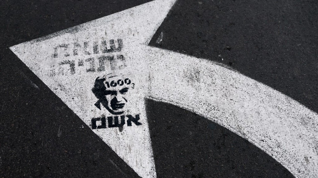 Un graffiti au pochoir représentant le Premier ministre israélien sortant, M. Netanyahou, est dessiné sur une flèche de signalisation le long d'une route devant le siège du ministère israélien de la défense, dans le centre de Tel Aviv, le 5 avril 2025.