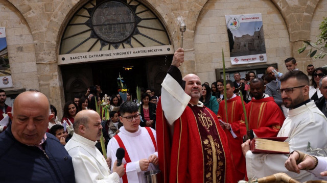Le prêtre palestinien de la paroisse latine de Bethléem, Rami Asakrieh (C), asperge d'eau bénite le dimanche des Rameaux devant la chapelle Sainte-Catherine, sur le côté nord de l'église de la Nativité, dans la ville biblique de Palestine occupée par Israël, le 13 avril 2025.