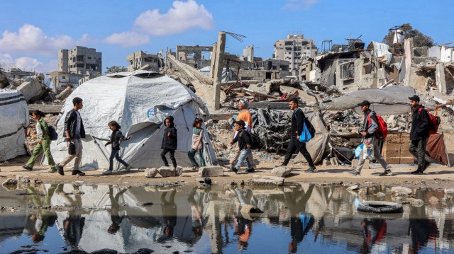 Des personnes passent devant une flaque d'eau près d'une tente-abri érigée près des décombres d'un bâtiment effondré dans le quartier de Nasr, dans l'ouest de la ville de Gaza, le 15 avril 2025.