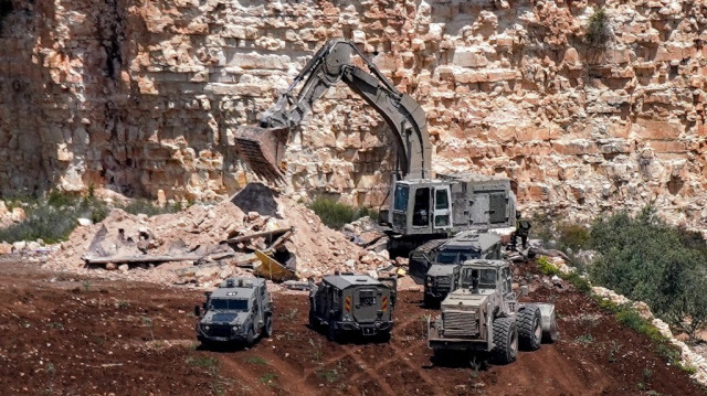 Une pelleteuse blindée de l'armée israélienne démolit une structure, après avoir tué deux personnes à l'intérieur, lors d'une opération de l'armée dans le village d'al-Misliyah, au sud de Jénine, dans le nord de la Palestine occupée, le 16 avril 2025.