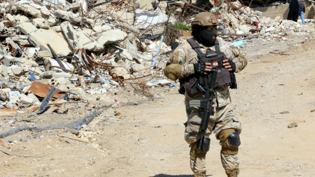 Un soldat libanais monte la garde devant un tas de décombres alors que les habitants inspectent leurs maisons détruites dans le village d'Adaisseh, au sud du Liban, le 18 février 2025.